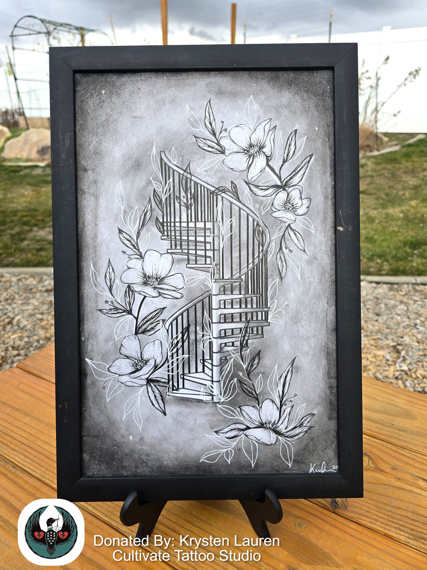 Framed artwork of a stylized twisting set of stairs with floral elements on a wooden surface.