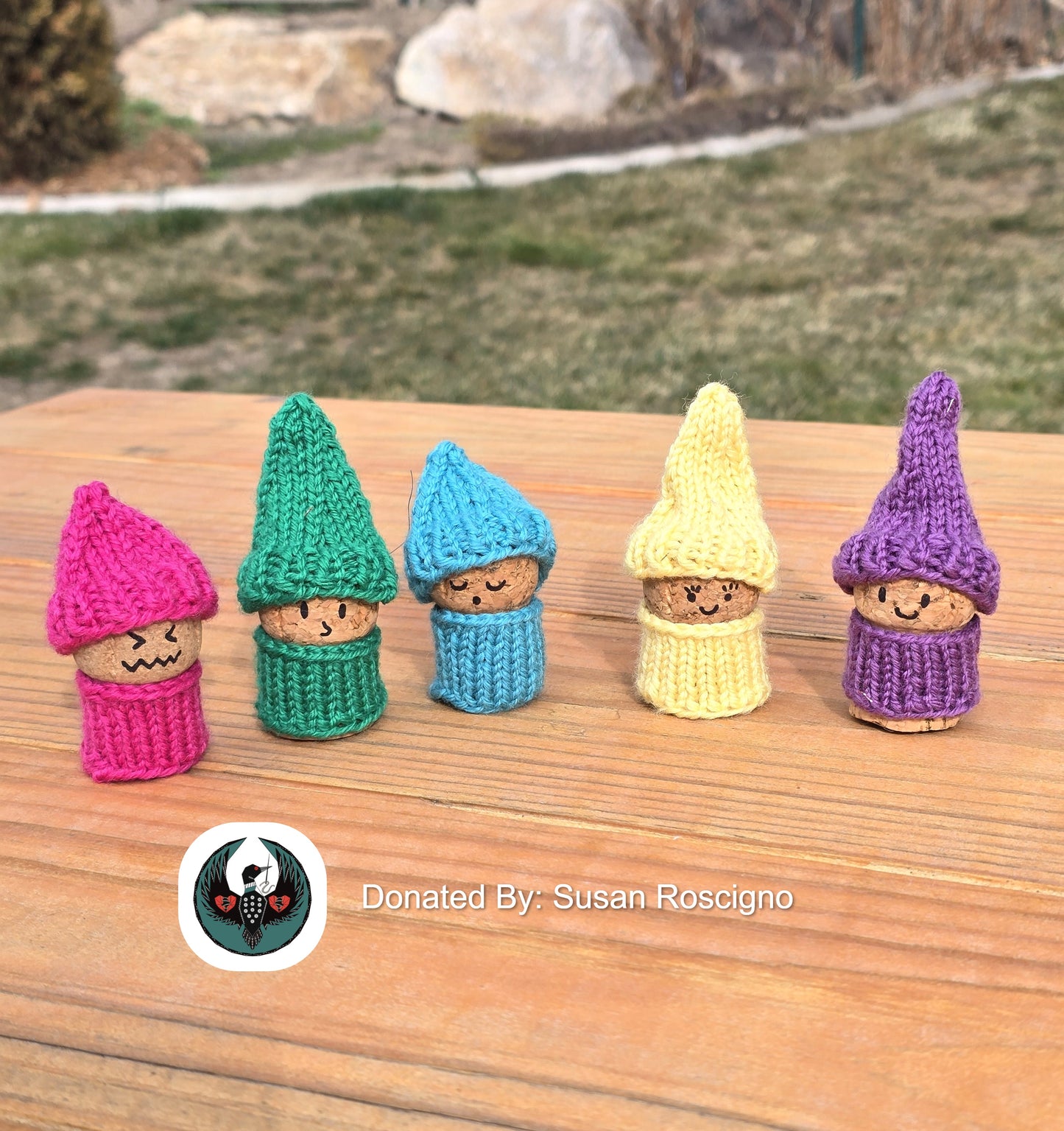 Five colorful knitted gnome figurines on a wooden surface with a blurred natural background.