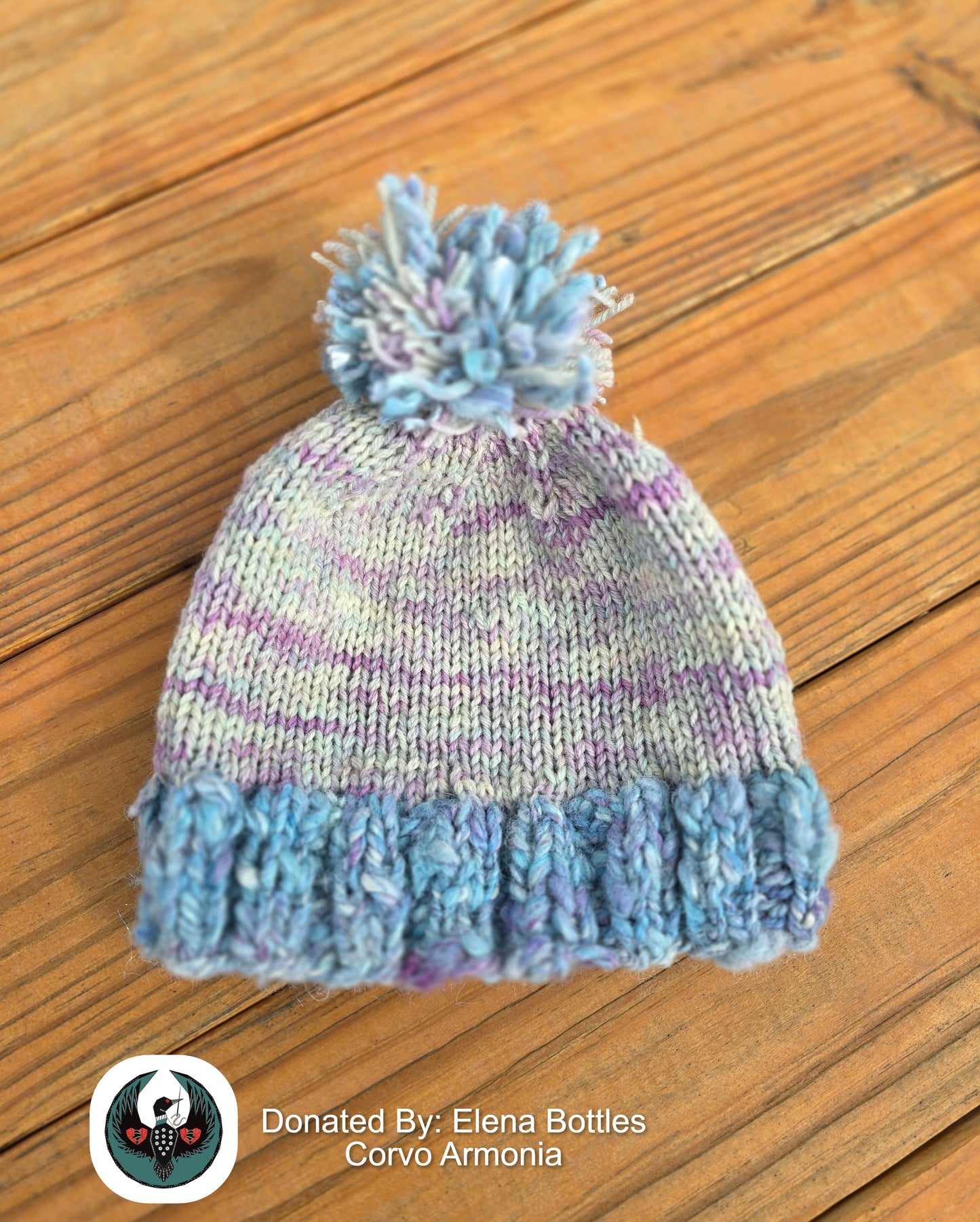 handknitted blue and pink beanie with a pompom top on a wooden background.
