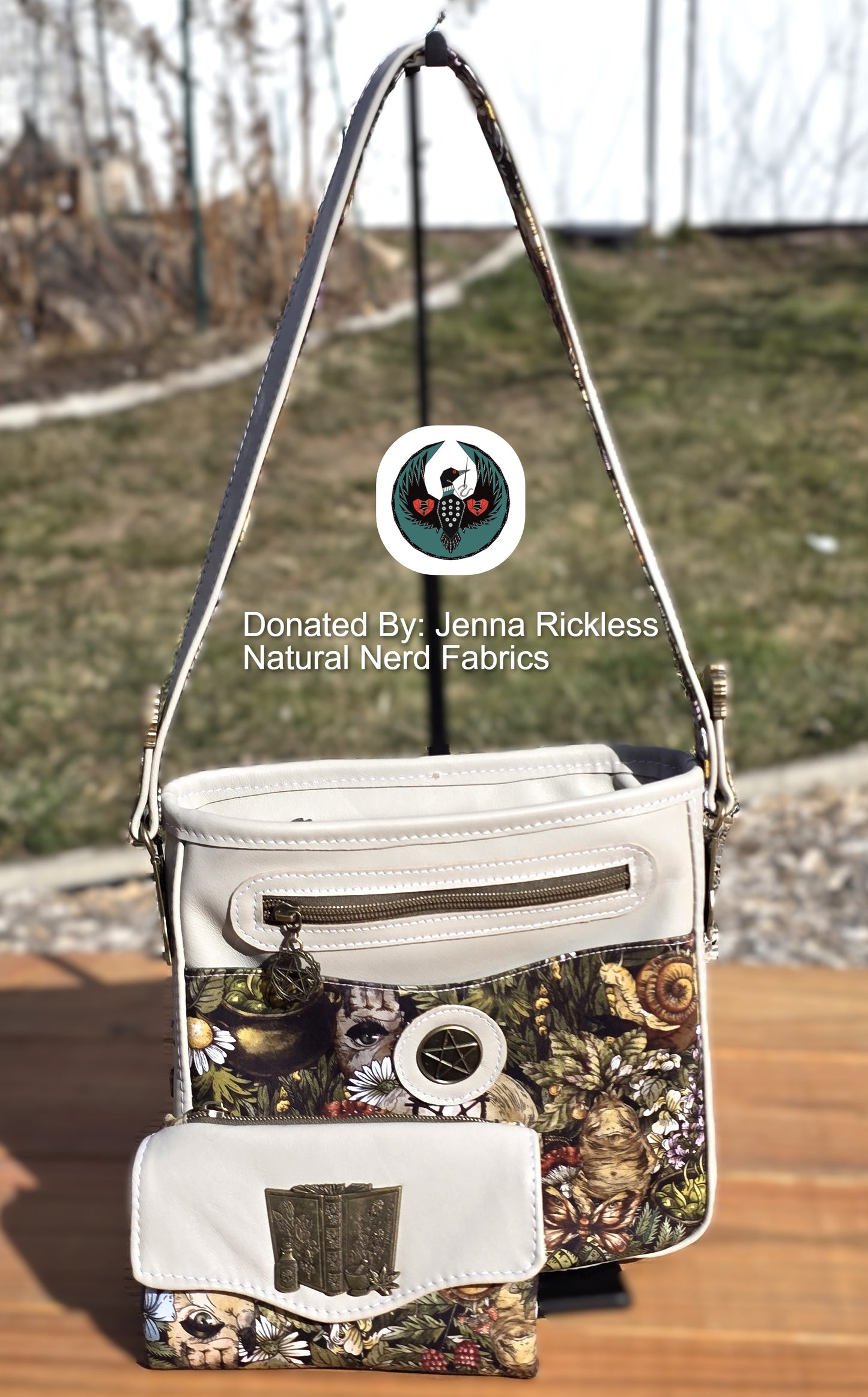 Cream leather handbag and wallet with a witchy nature-themed pattern and bronze hardware on a wooden surface