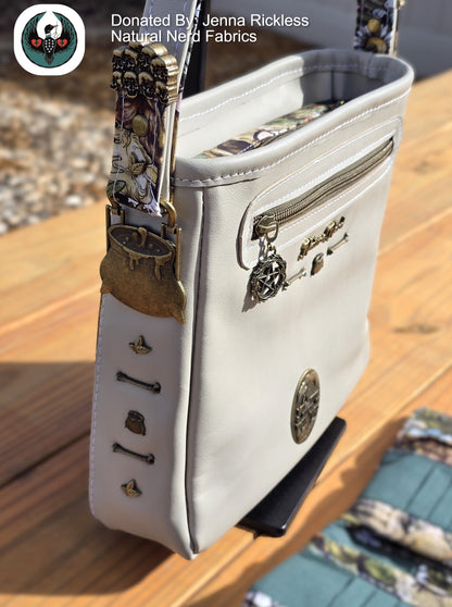cream leather heandbag viewed from the side with bronze hardware detailing including cauldrons, bones, and leaves.