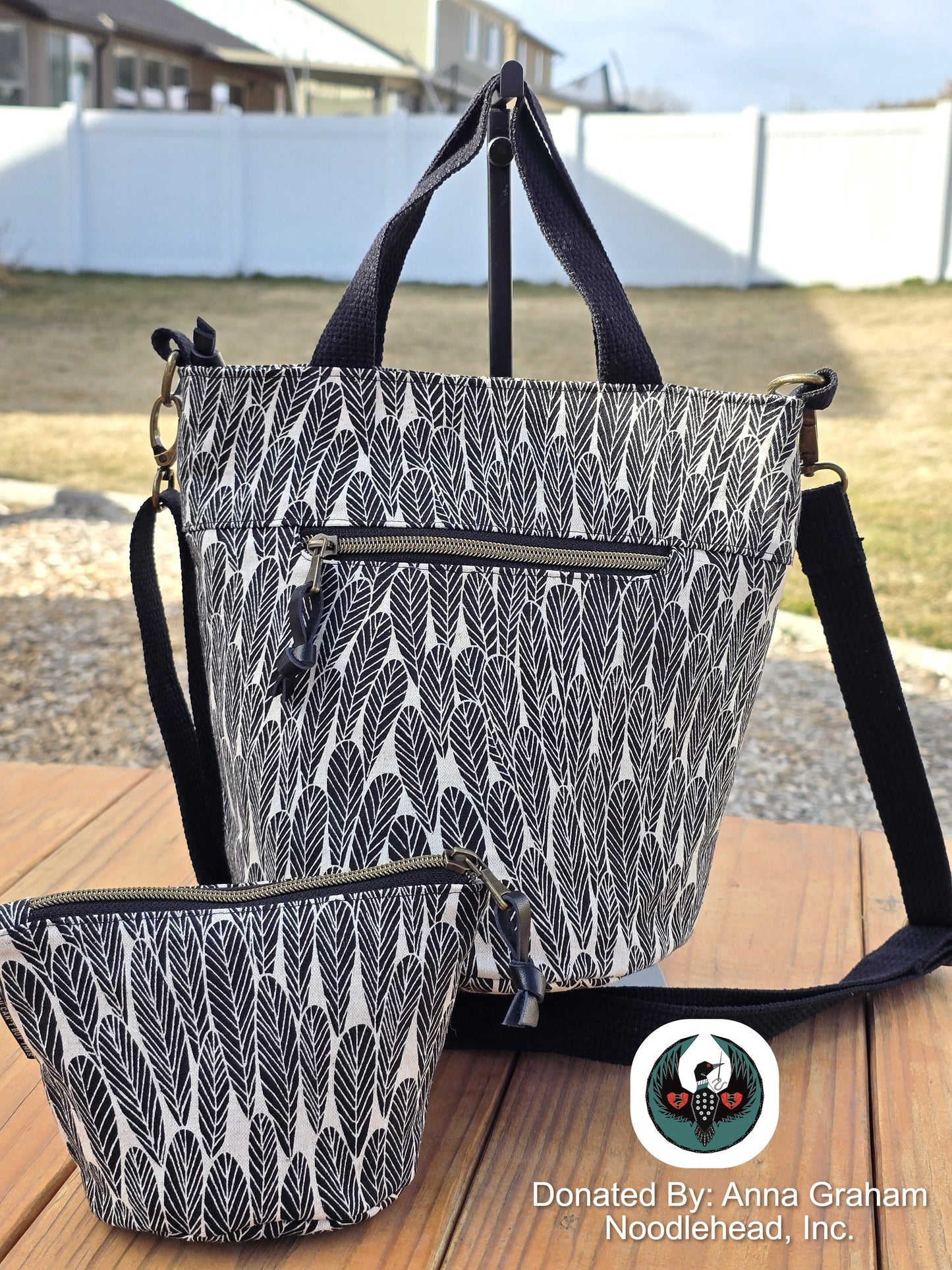 Black and white patterned tote bag with matching pouch on a wooden surface outdoors.