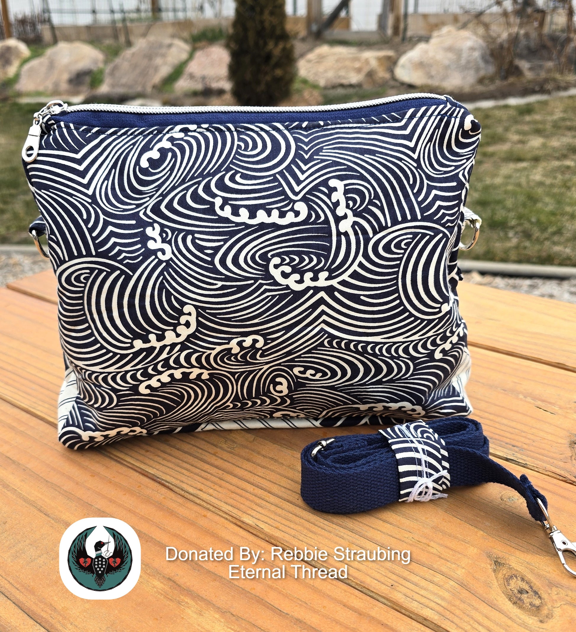 Blue and white patterned bag with strap on a wooden surface, outdoors.