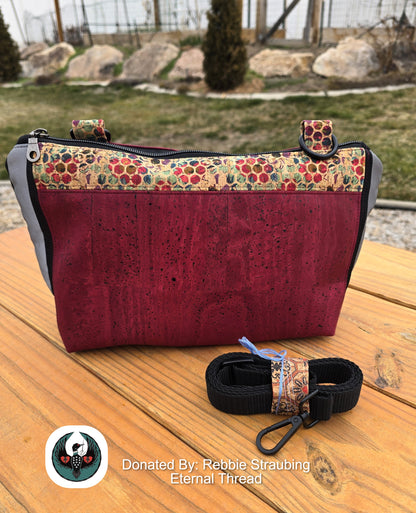 red and hexa dot cork handbag with a black crossbody strap on a wooden table