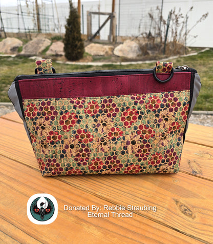 red and hexa dot cork handbag with a black crossbody strap on a wooden table