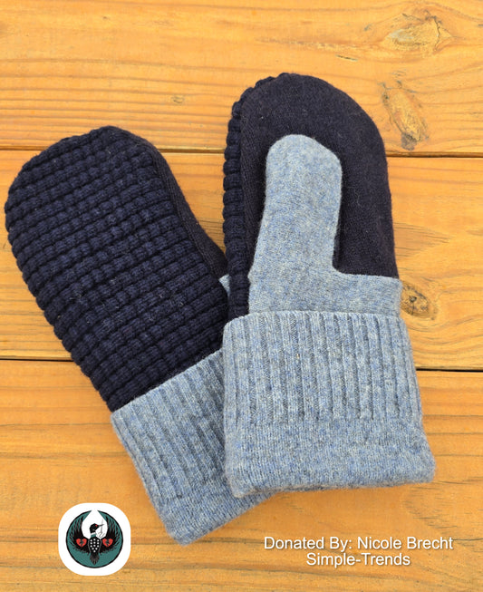 Pair of navy and gray wool mittens on a wooden surface with a donation label.