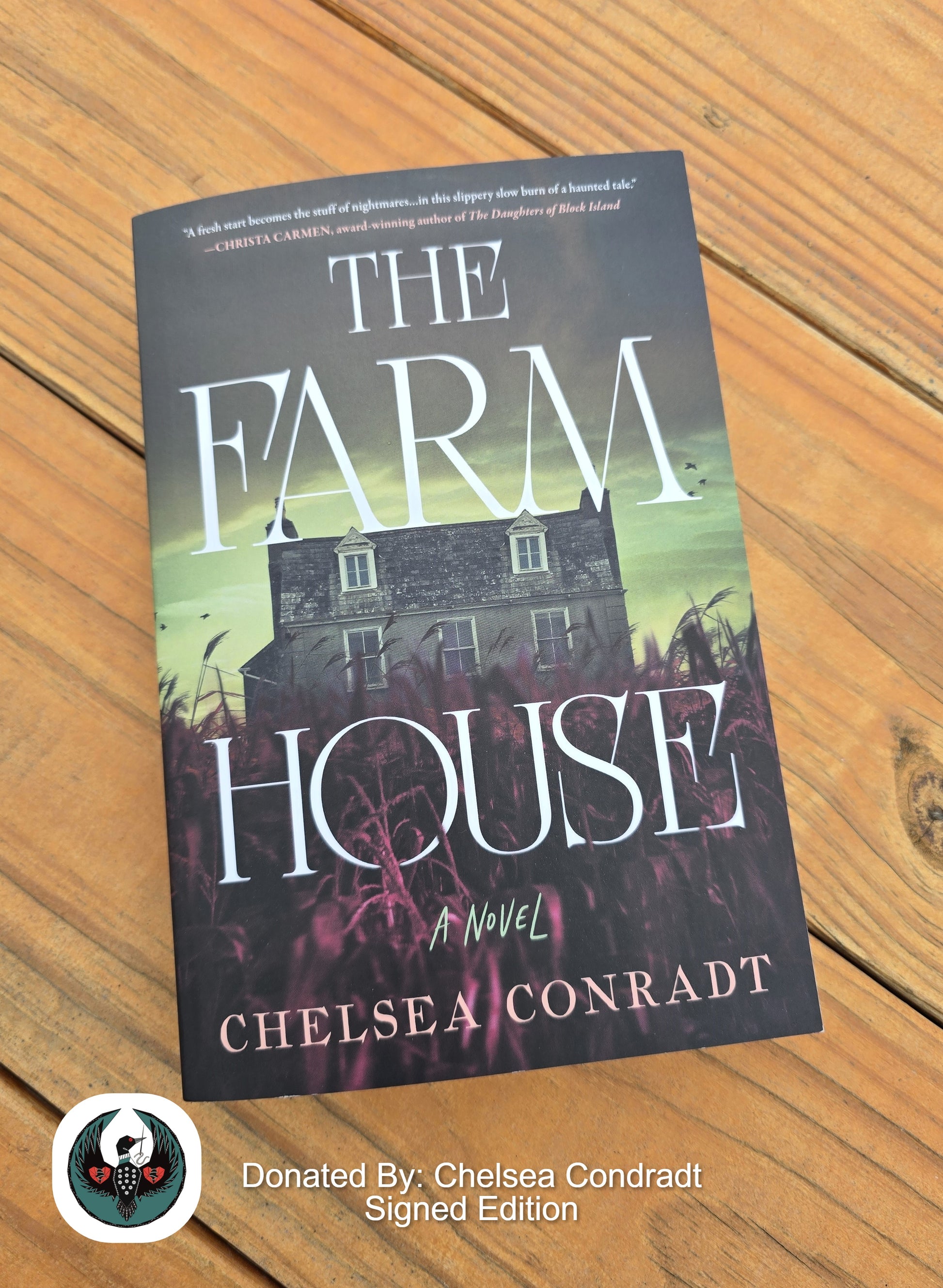 Book titled 'The Farmhouse' by Chelsea Conradt on a wooden surface