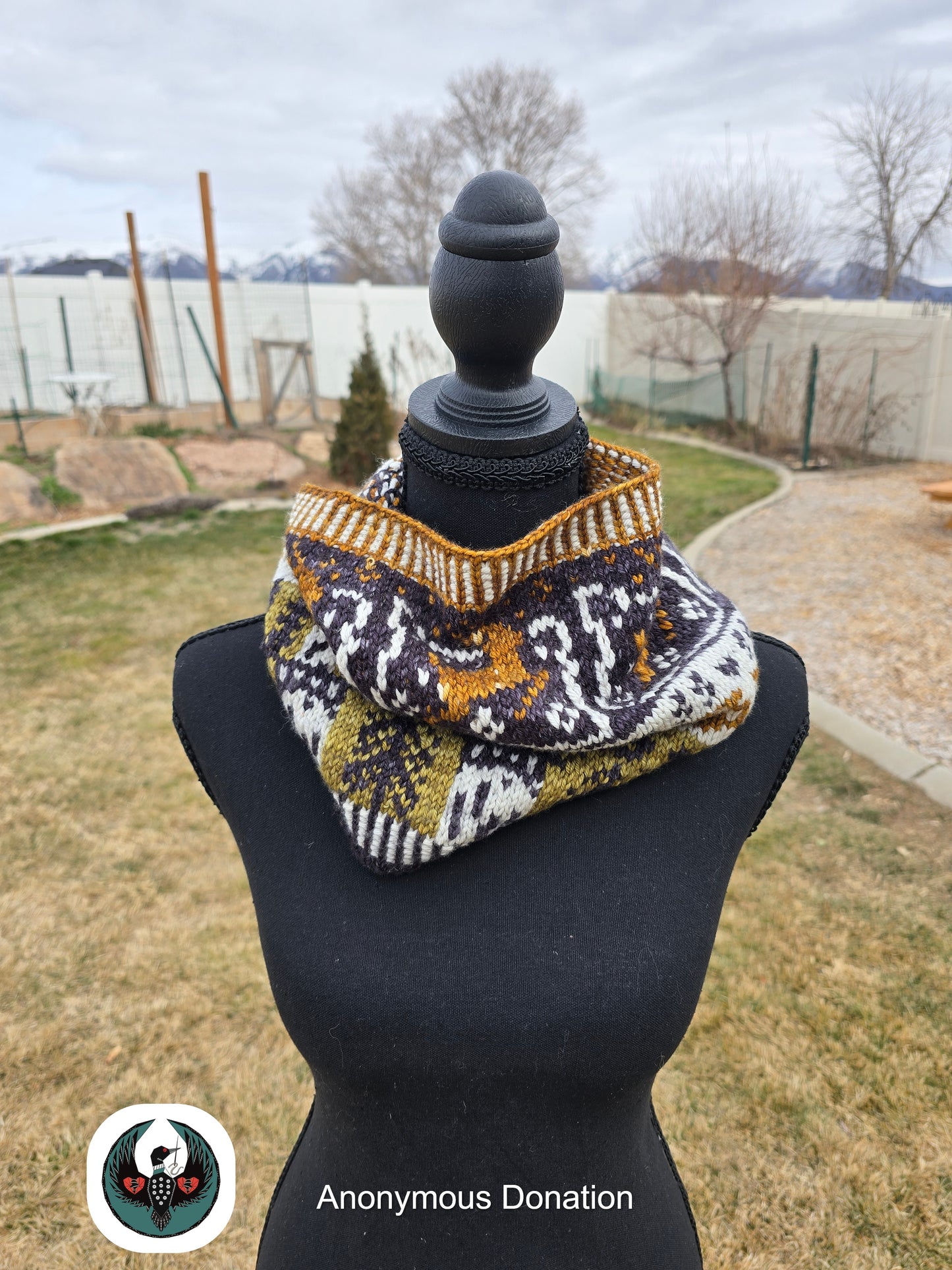 Knitted cowl with geometric pattern on a mannequin against an outdoor background