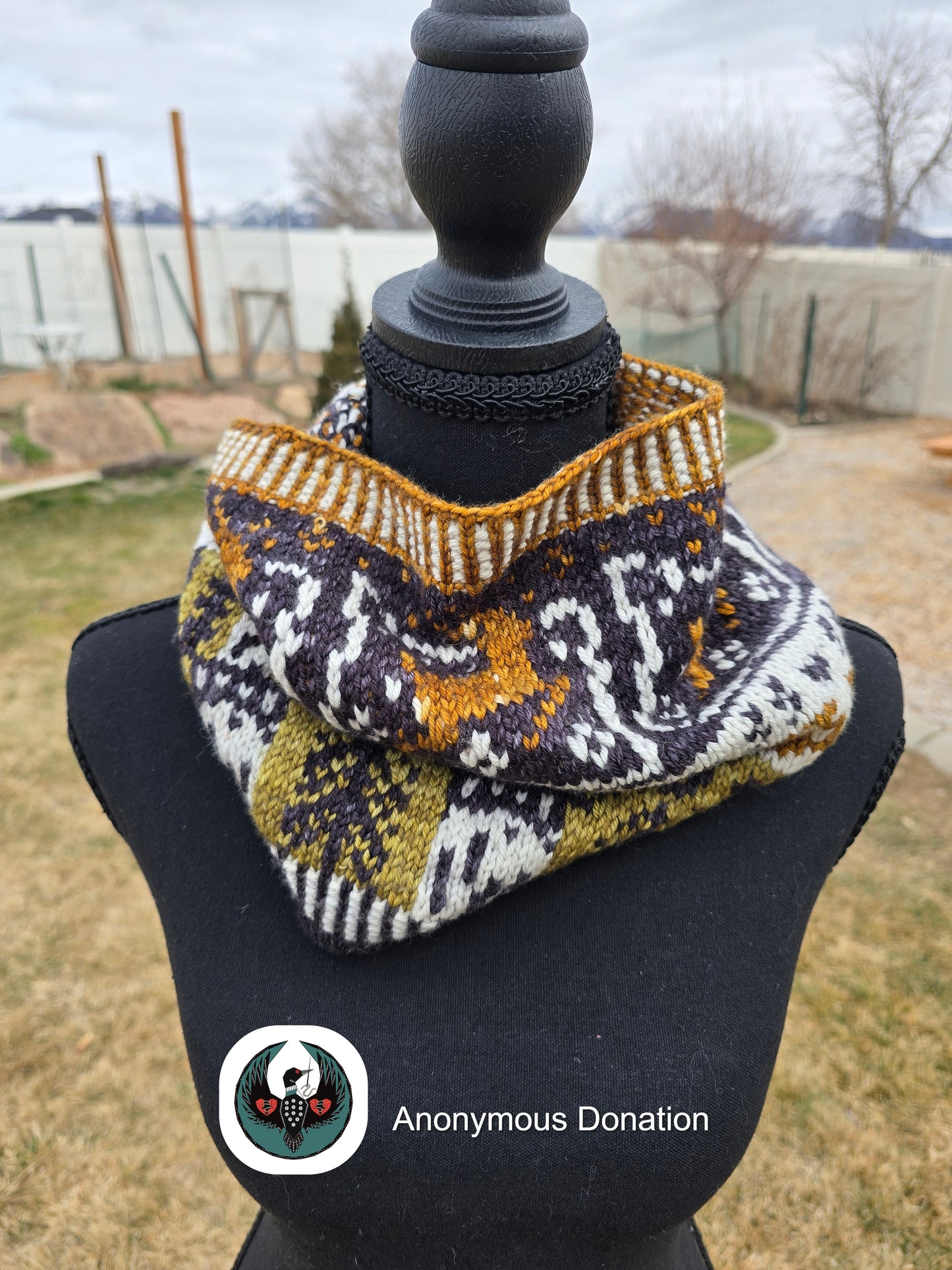 Knitted cowl with geometric pattern on a mannequin against an outdoor background