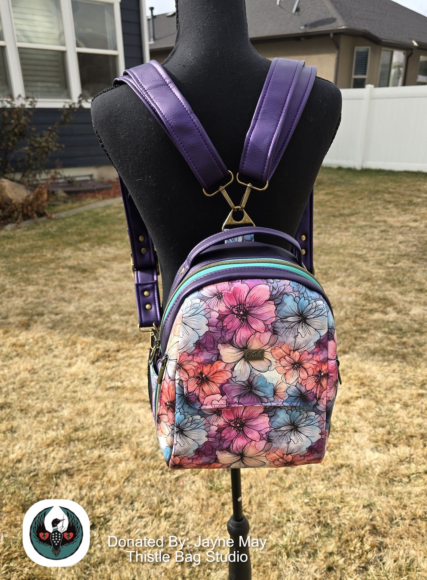 Floral-patterned backpack with purple straps on a mannequin outdoors.