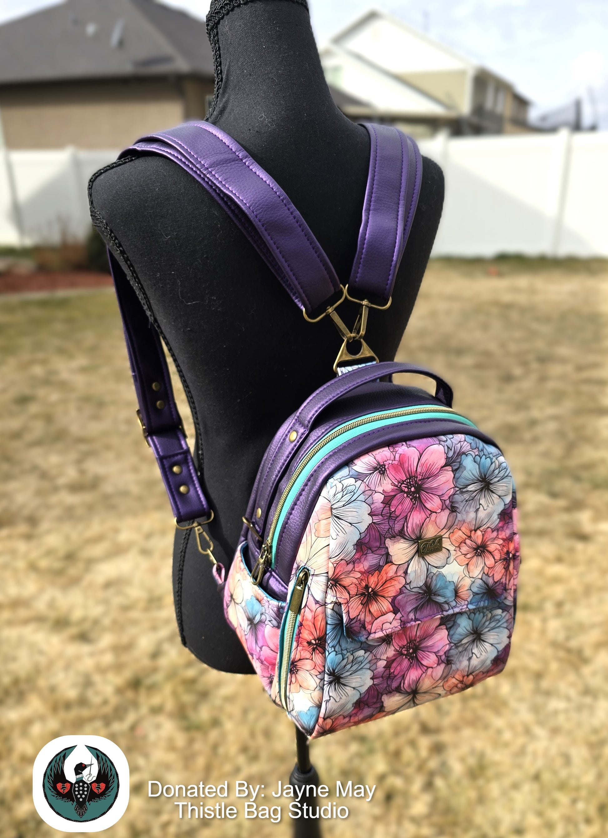 Floral-patterned backpack with purple straps on a mannequin outdoors.