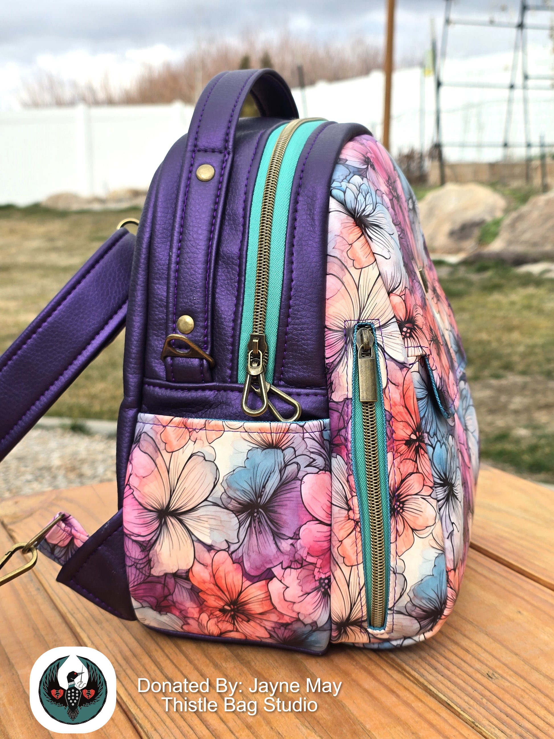 Floral-patterned backpack with purple accents on a wooden surface