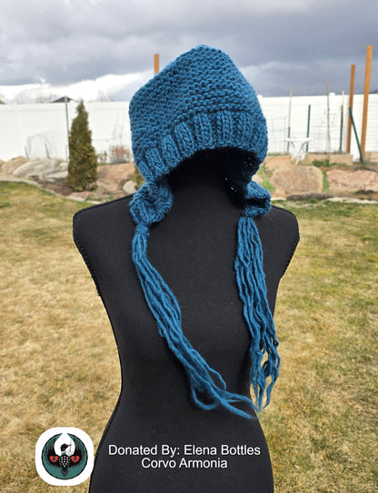 Teal knitted wool hat with long tassels on a mannequin against an outdoor background