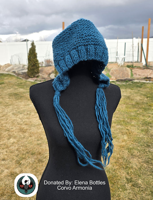 Teal knitted wool hat with long tassels on a mannequin against an outdoor background