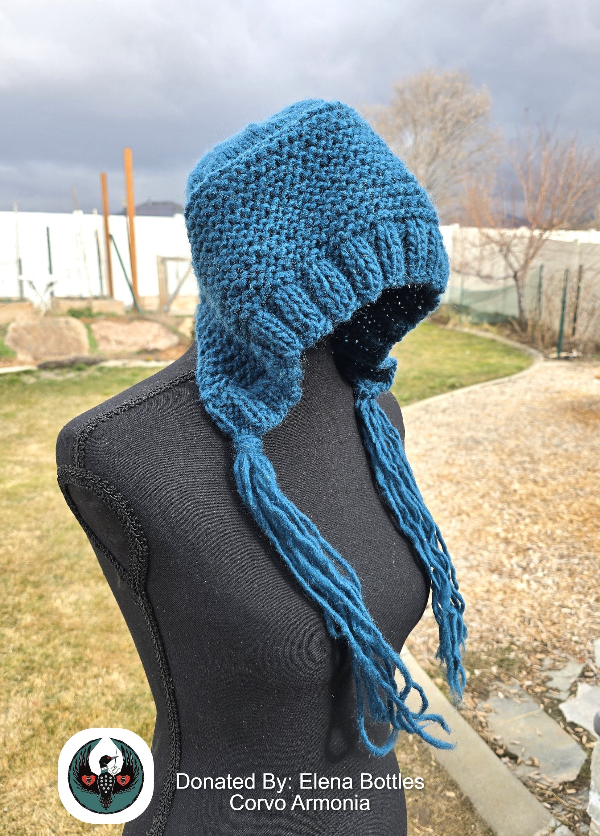 Teal knitted wool hat with long tassels on a mannequin against an outdoor background