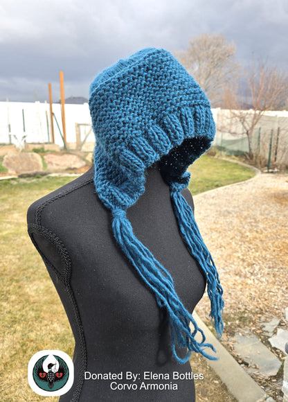 Teal knitted wool hat with long tassels on a mannequin against an outdoor background