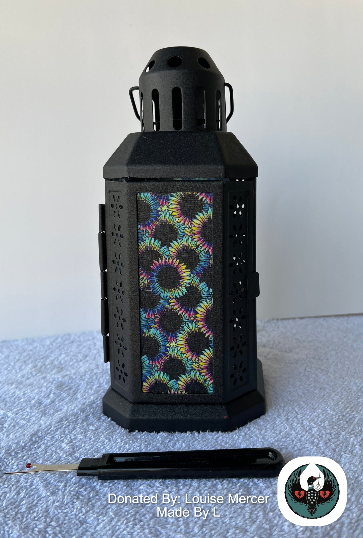 Black lantern with colorful floral pattern on a white surface, donated by Louise Mercer.