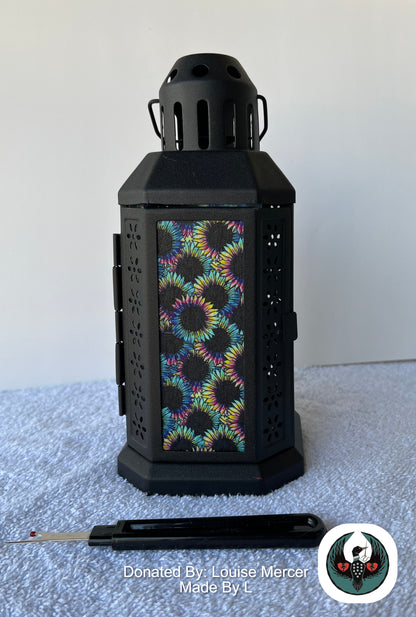 Black lantern with colorful floral pattern on a white surface, donated by Louise Mercer.