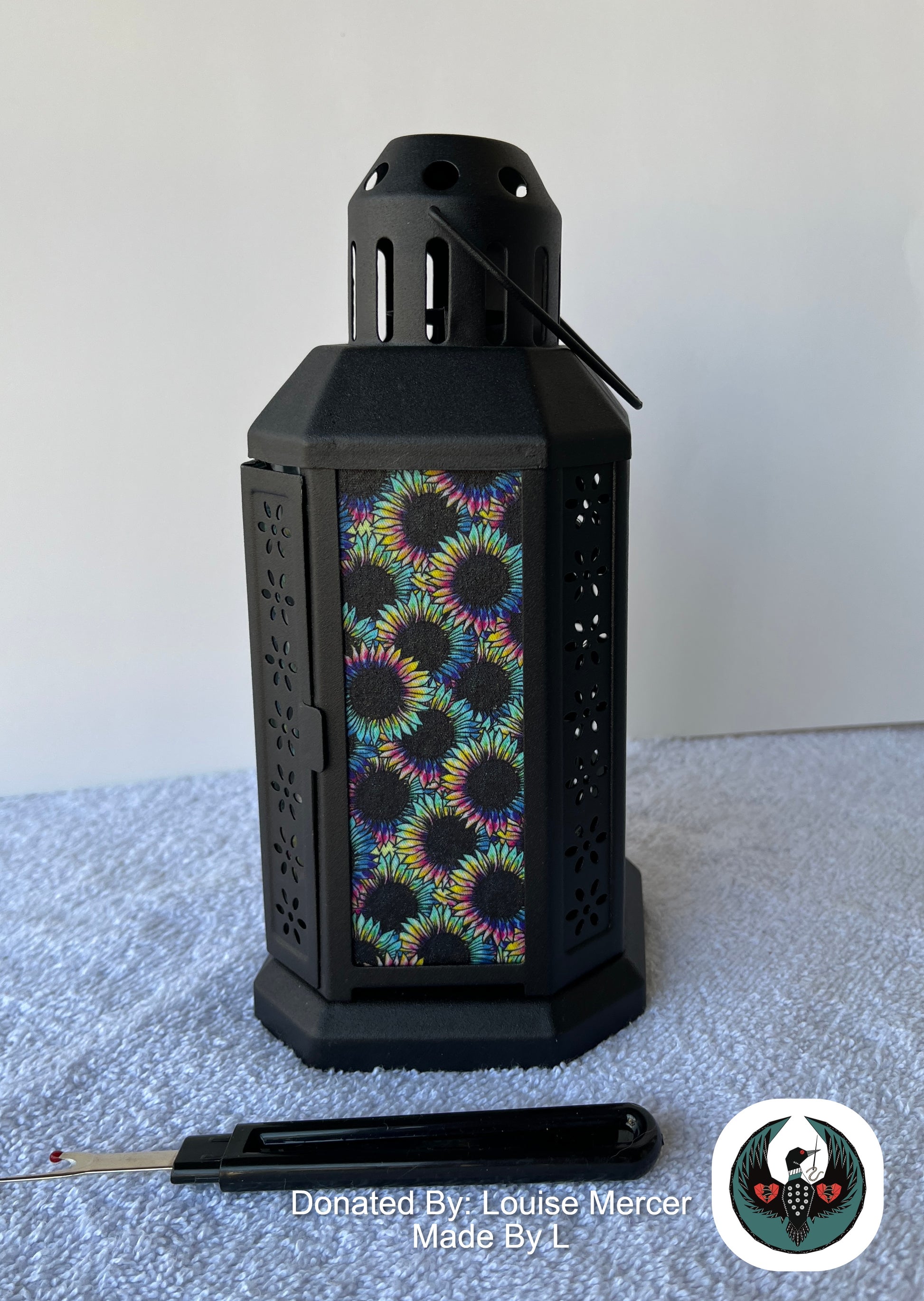 Black lantern with colorful floral pattern on a white surface, donated by Louise Mercer.